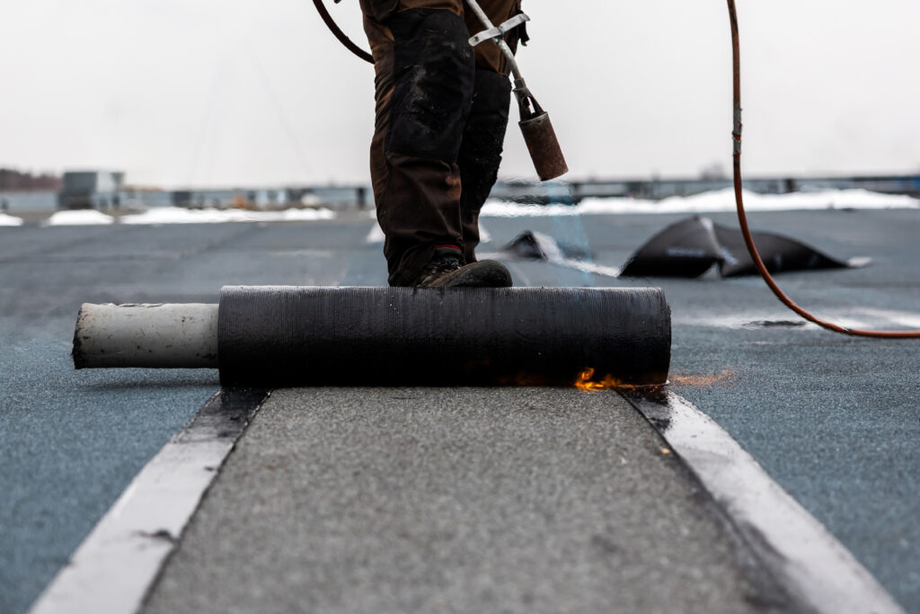 Commercial flat roof installation using professional blowtorch welding.